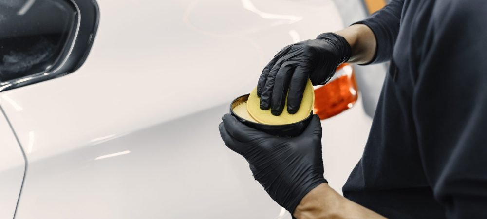 Man polish a car in a garage Man in a garage. Worker polish a car. Man in a black uniform.